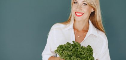 Cheerful woman with blonde hair holding fresh lettuce, promoting healthy living in a studio setting.