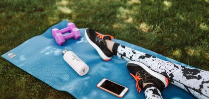 Focused workout setup outdoors with mat, dumbbells, phone, and water bottle.